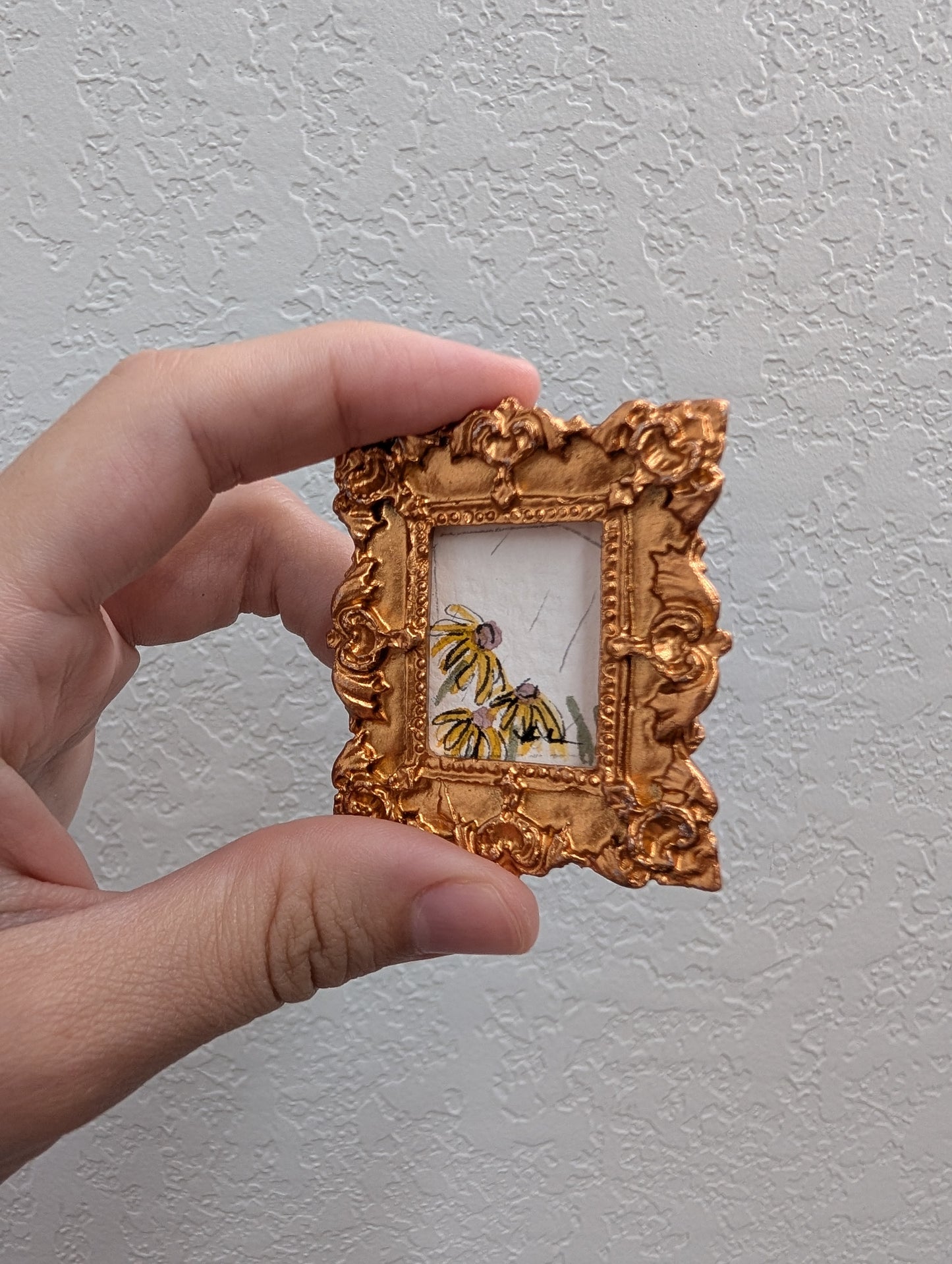 a hand holding a small picture frame with a picture of a bee on it