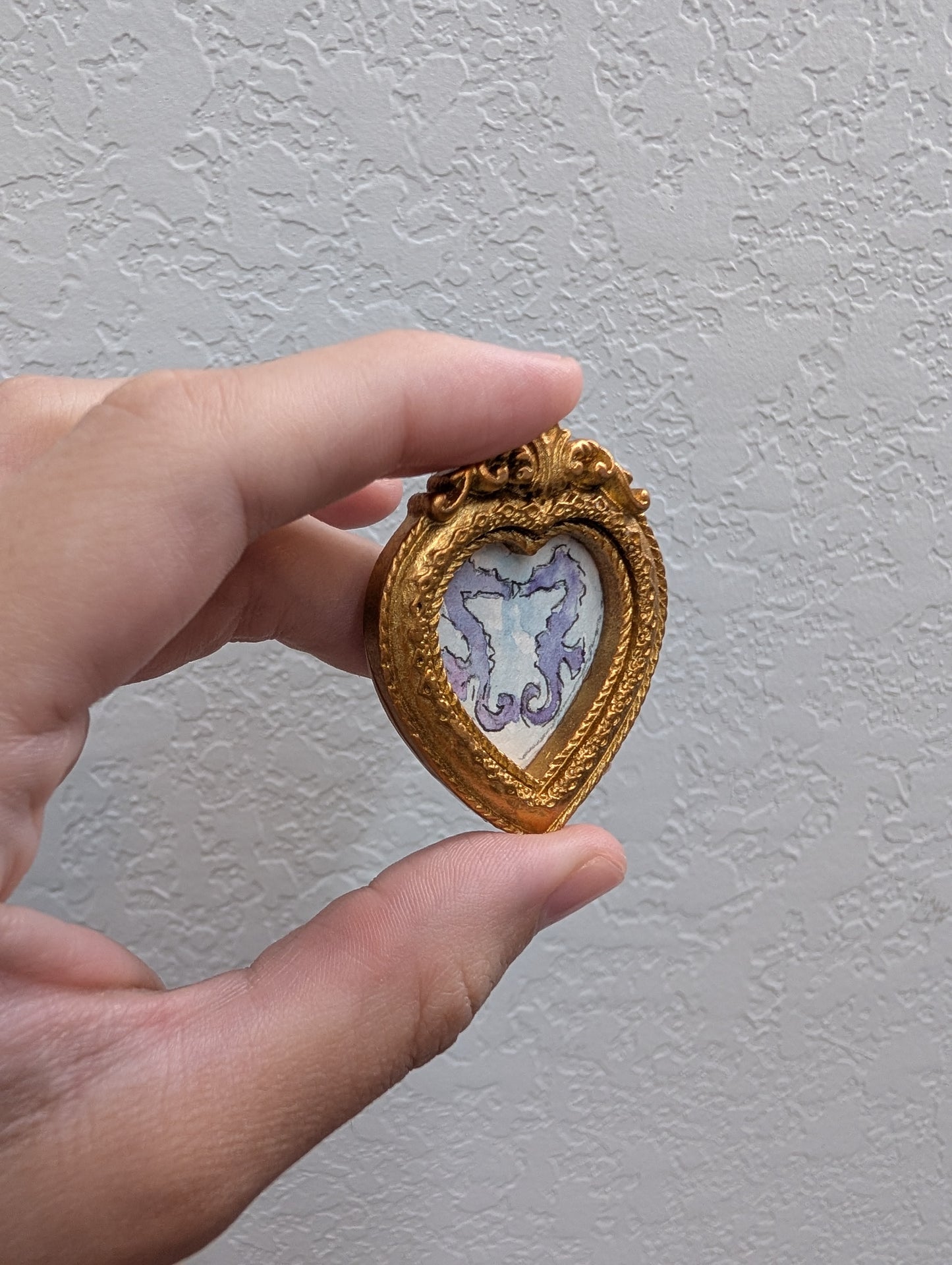 a hand holding a small gold heart shaped brooch