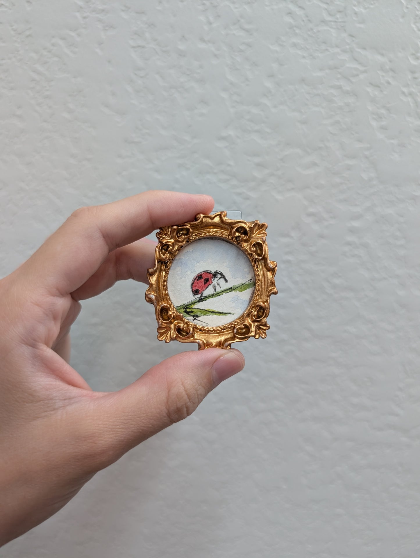 a hand holding a miniature picture of a ladybug