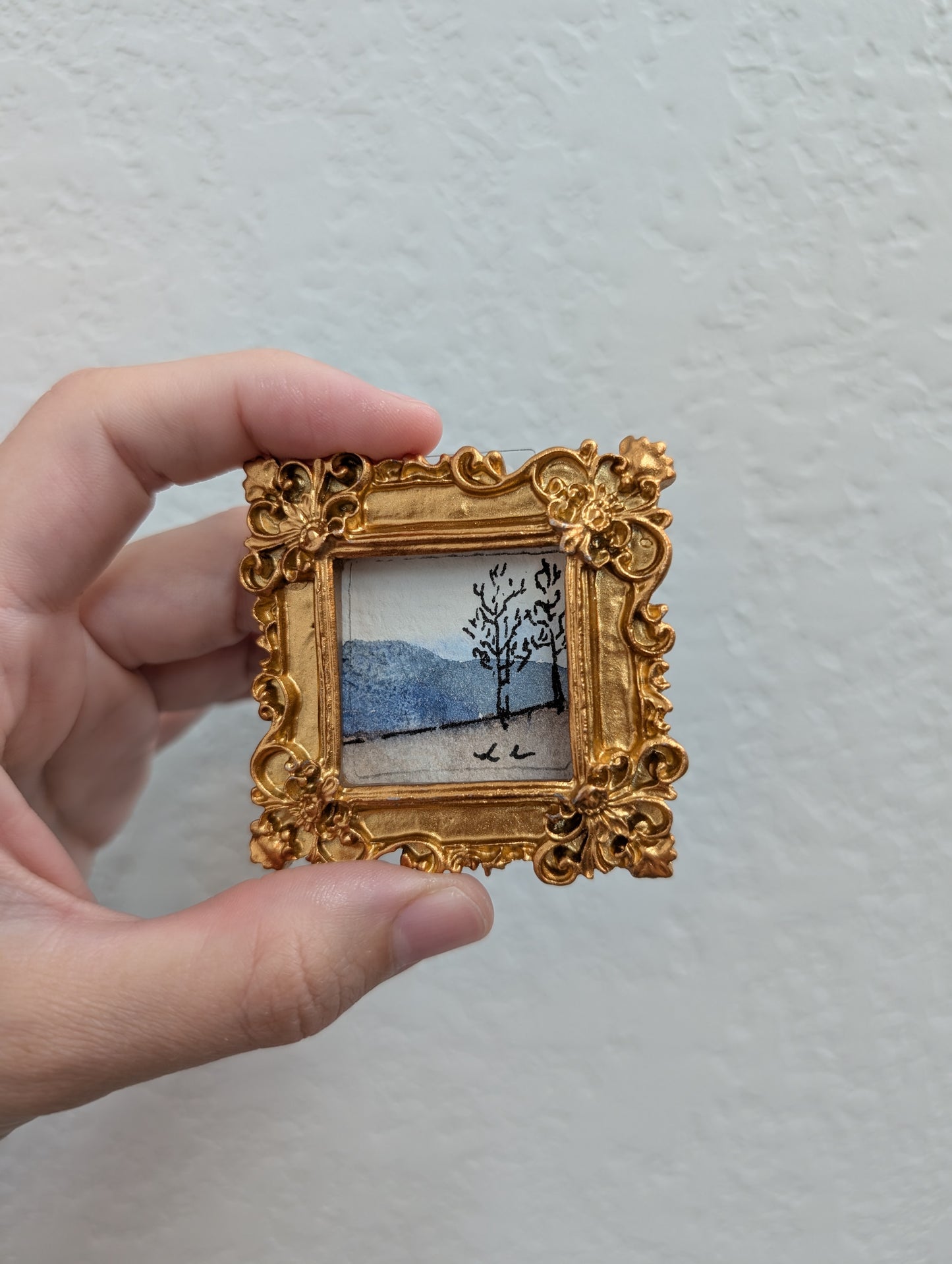 a person holding a small picture frame with a painting on it