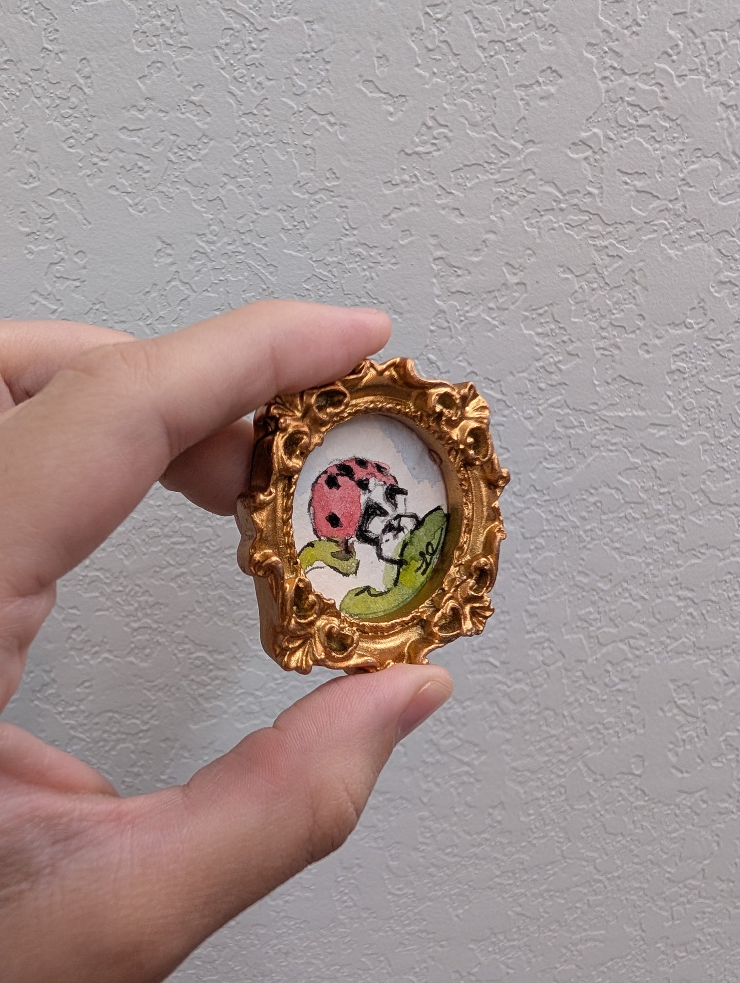 a hand holding a small picture frame with a ladybug on it