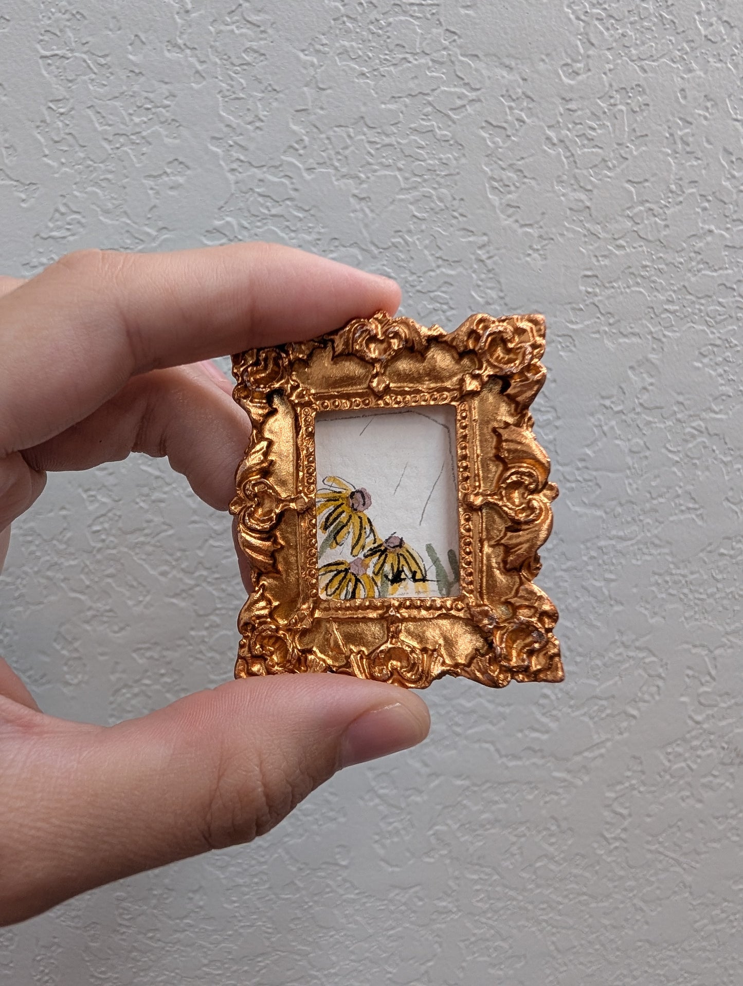 a person holding a small gold frame with a painting on it