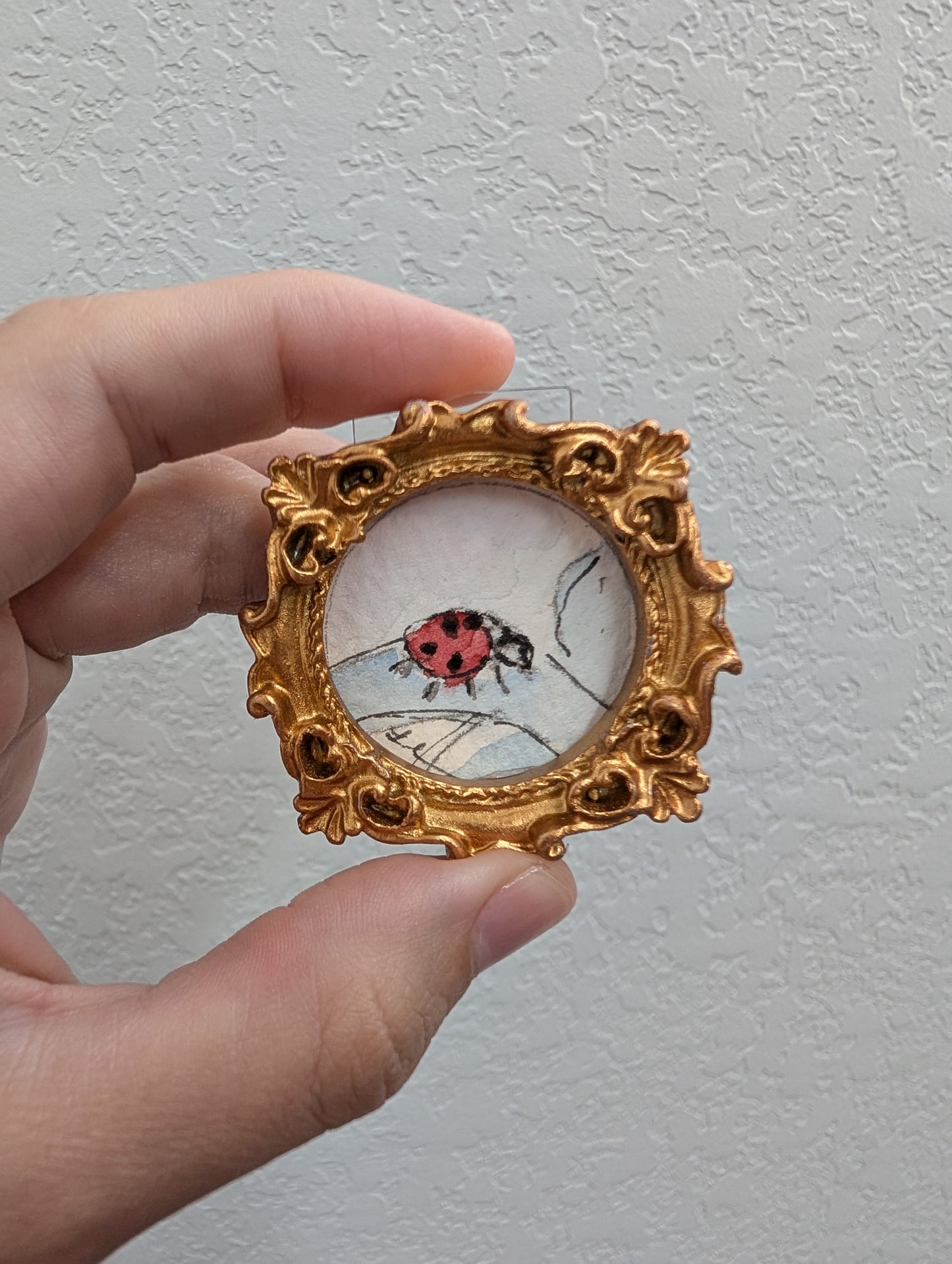 a hand holding a miniature picture of a ladybug