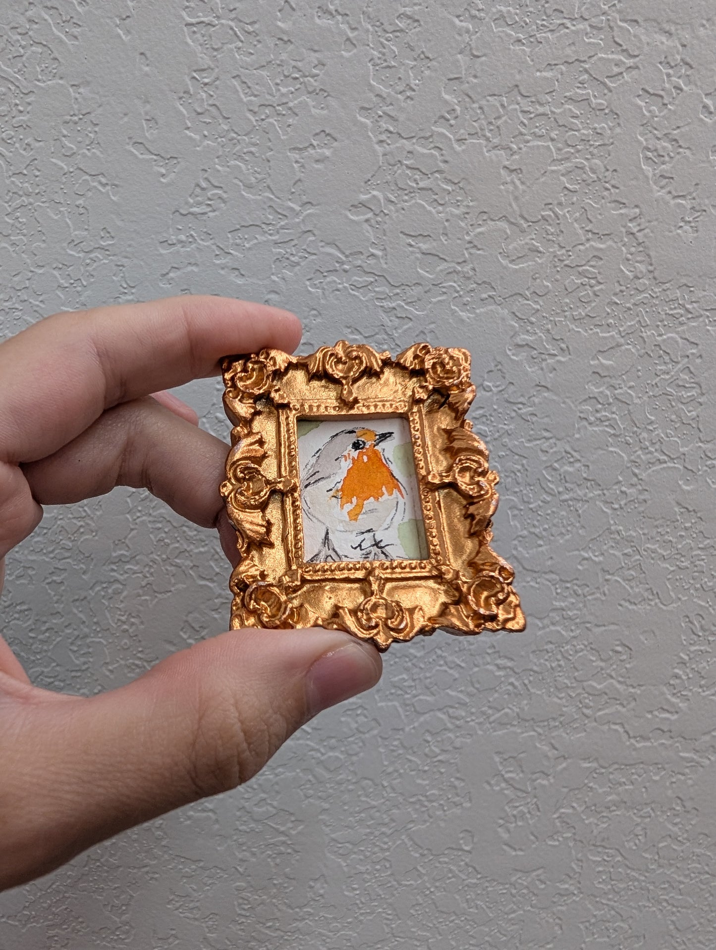a hand holding a miniature picture frame with a picture of a bird on it