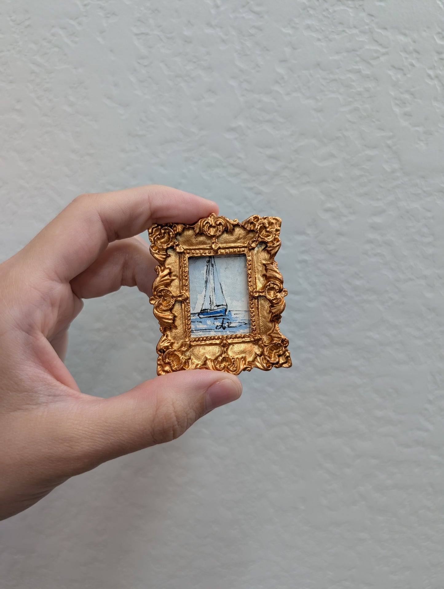 a hand holding a miniature picture frame with a boat on it