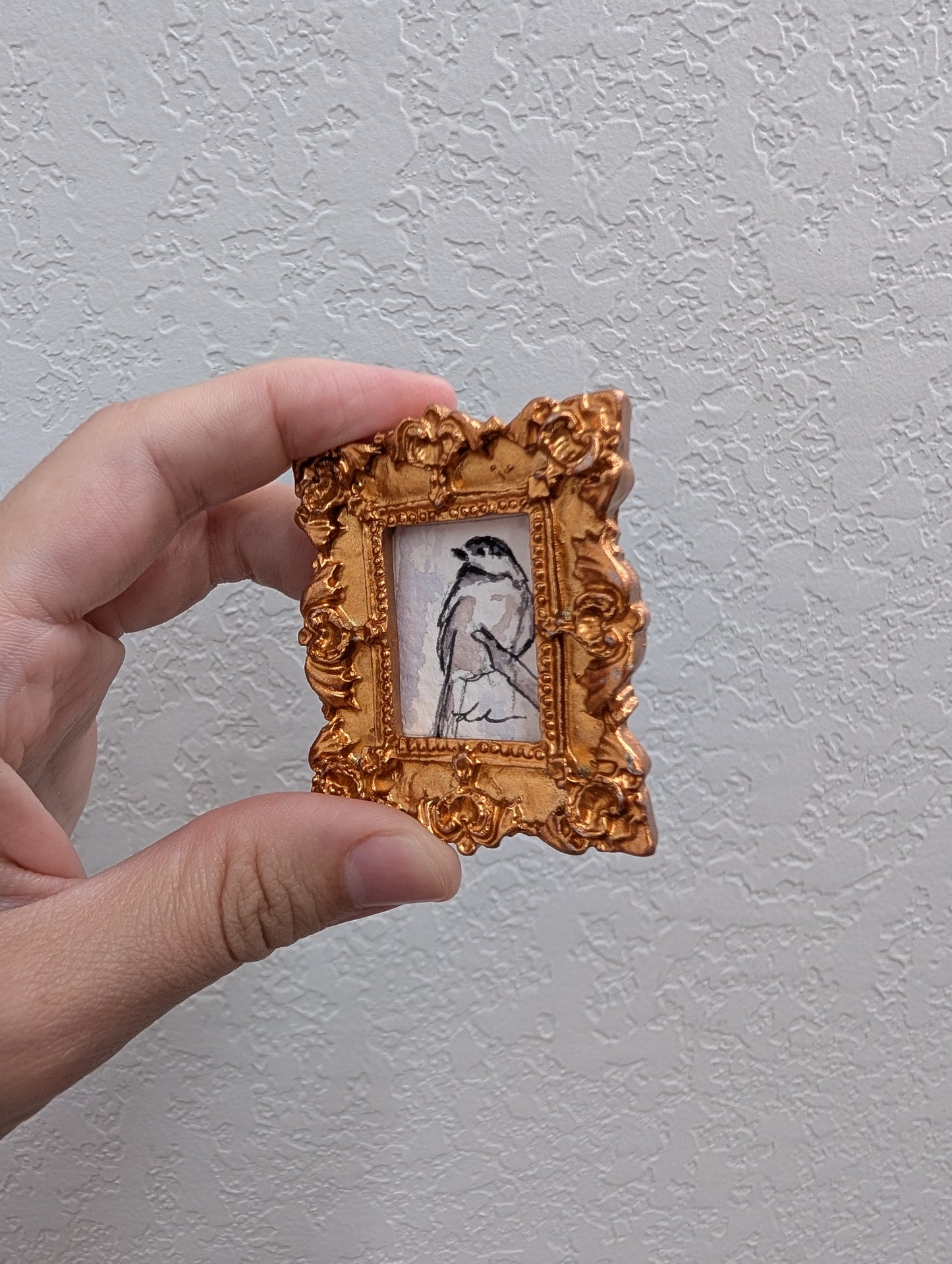 a hand holding a small picture frame with a bird on it