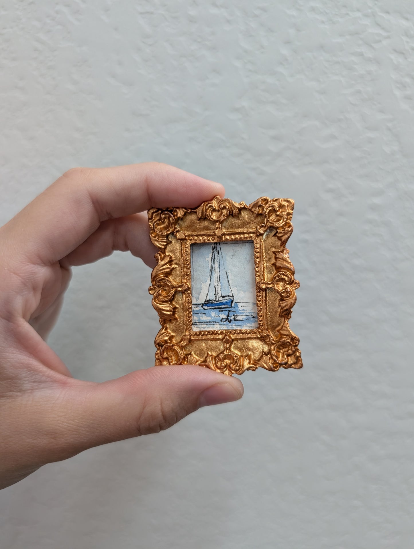 a person holding a small picture frame with a sailboat on it