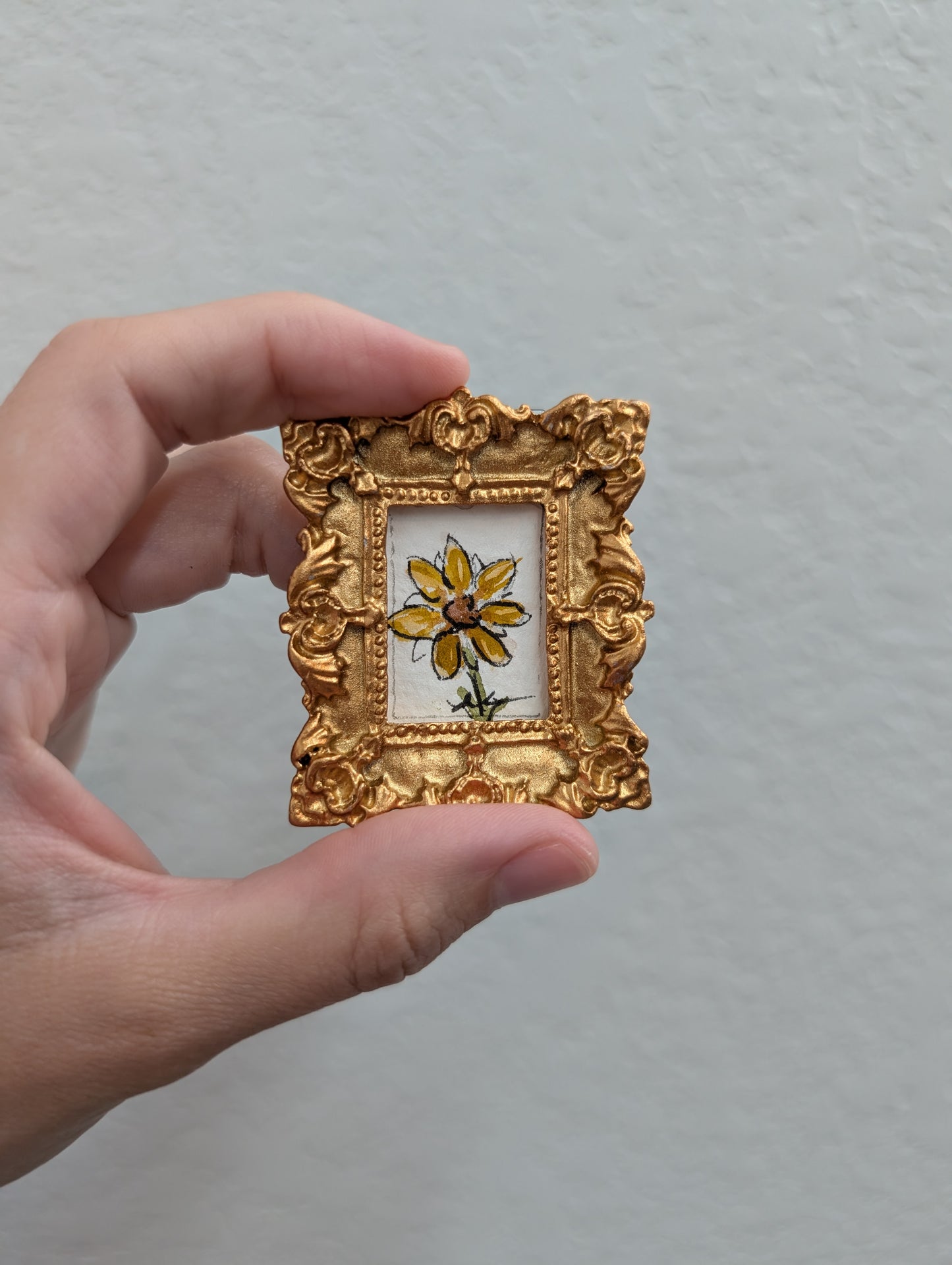 a person holding a small picture frame with a flower painted on it