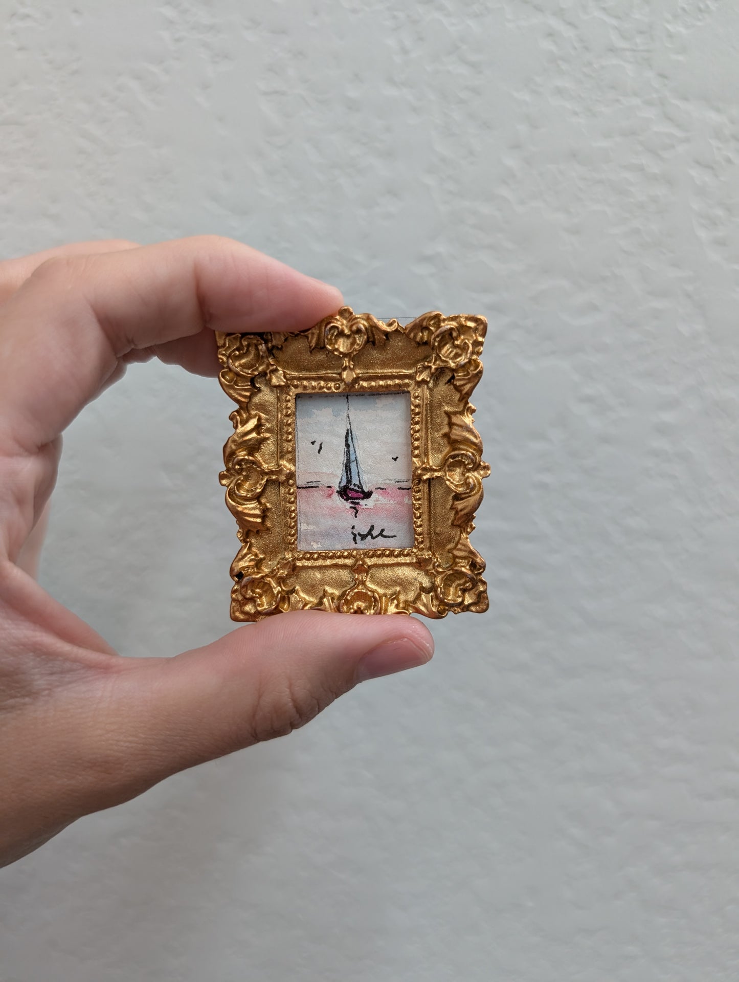 a person holding a small picture frame with a sailboat on it