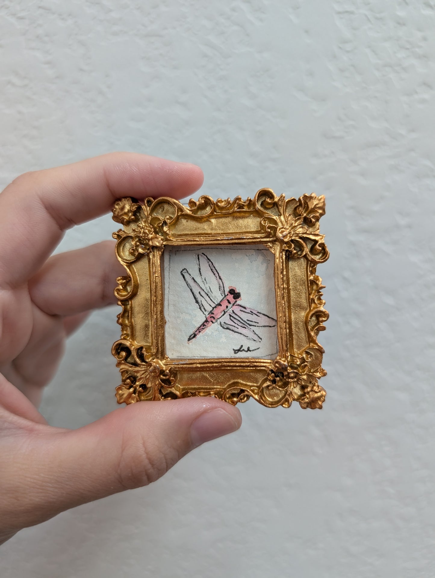 a hand holding a miniature picture frame with a bird on it