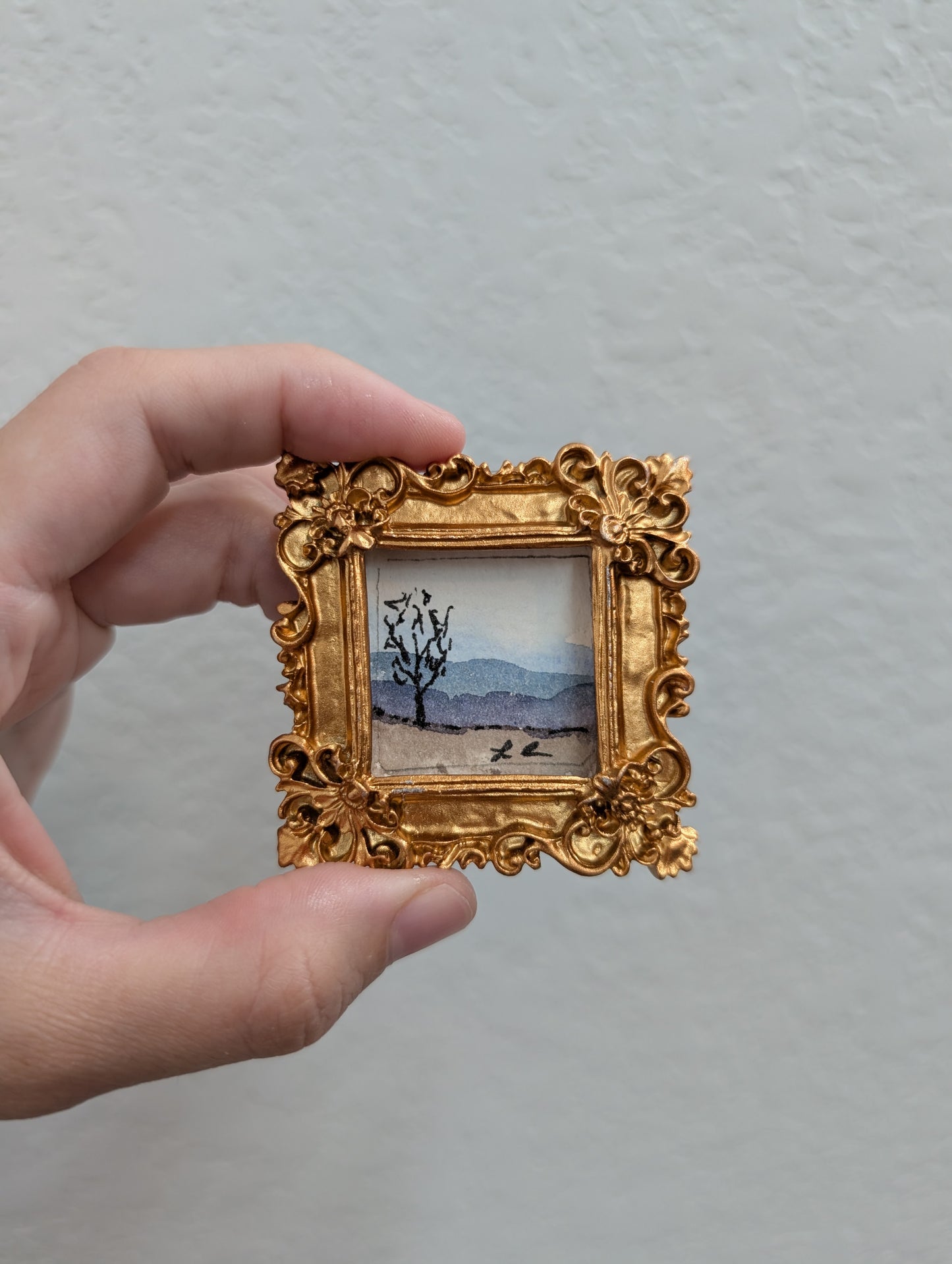 a person holding a picture of a tree in a gold frame