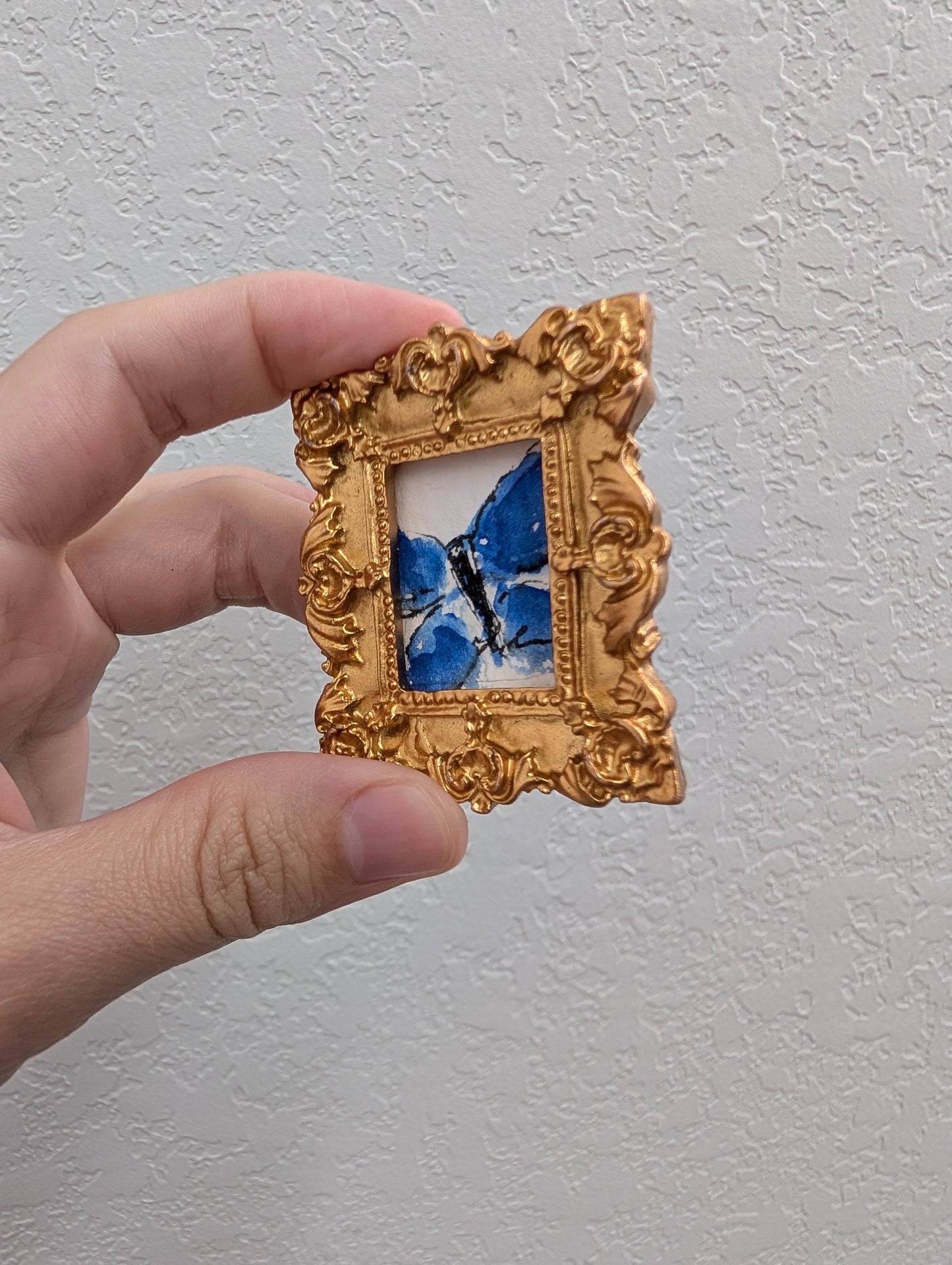 a hand holding a small picture frame with a blue bird on it