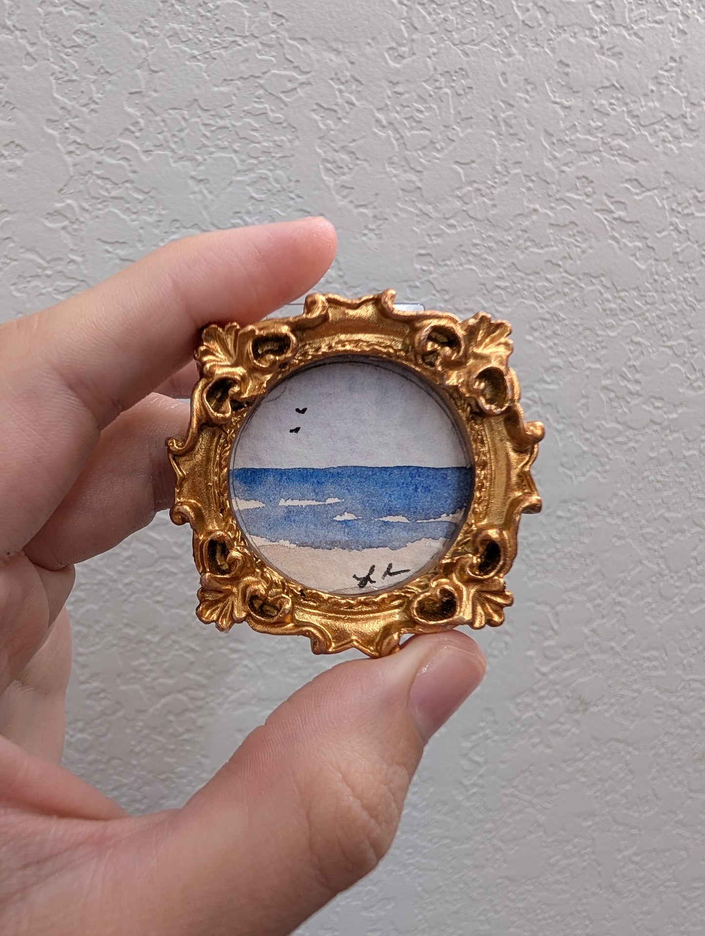 a hand holding a miniature picture of a beach