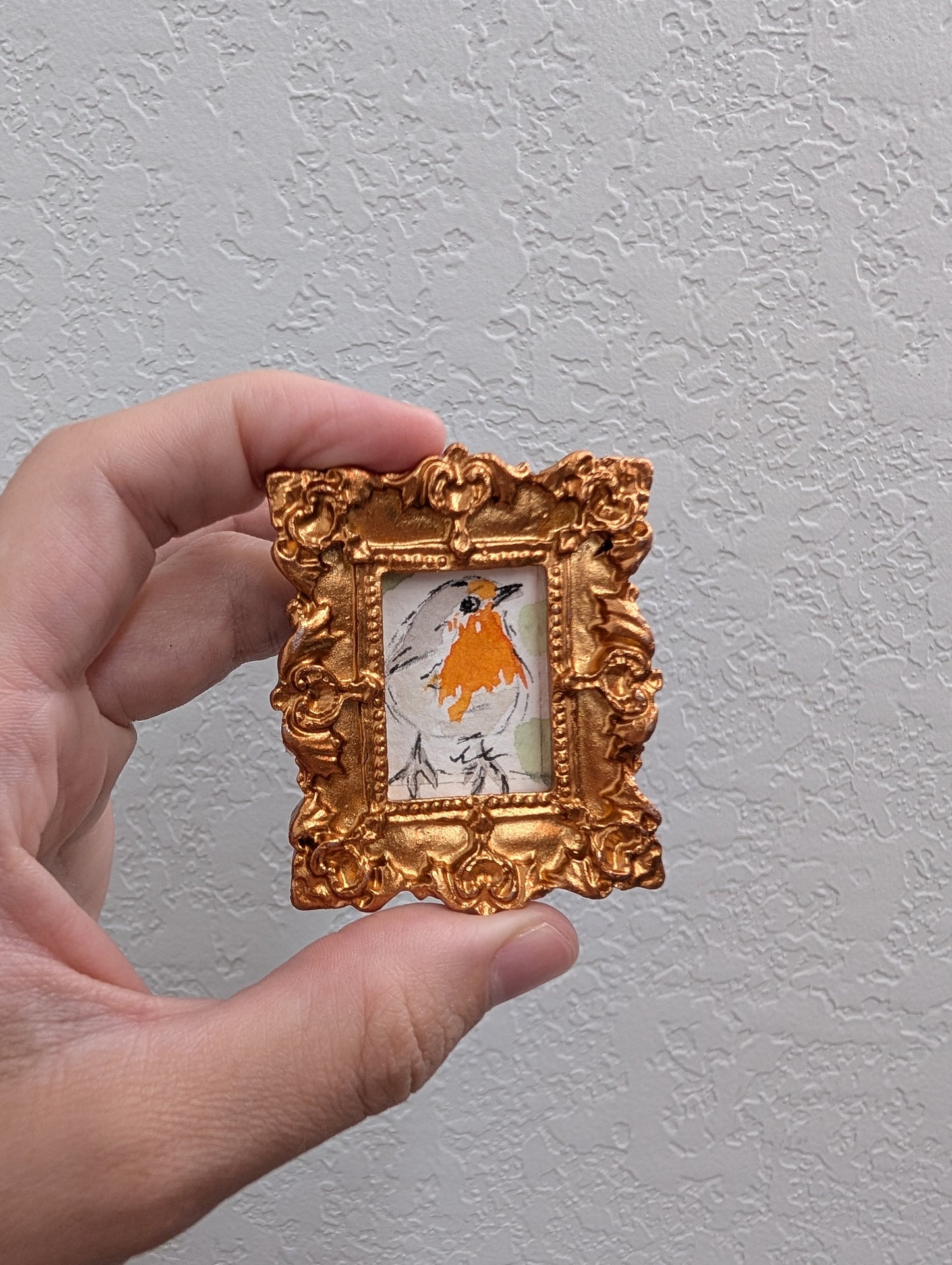 a hand holding a miniature picture frame with a picture of a bird on it