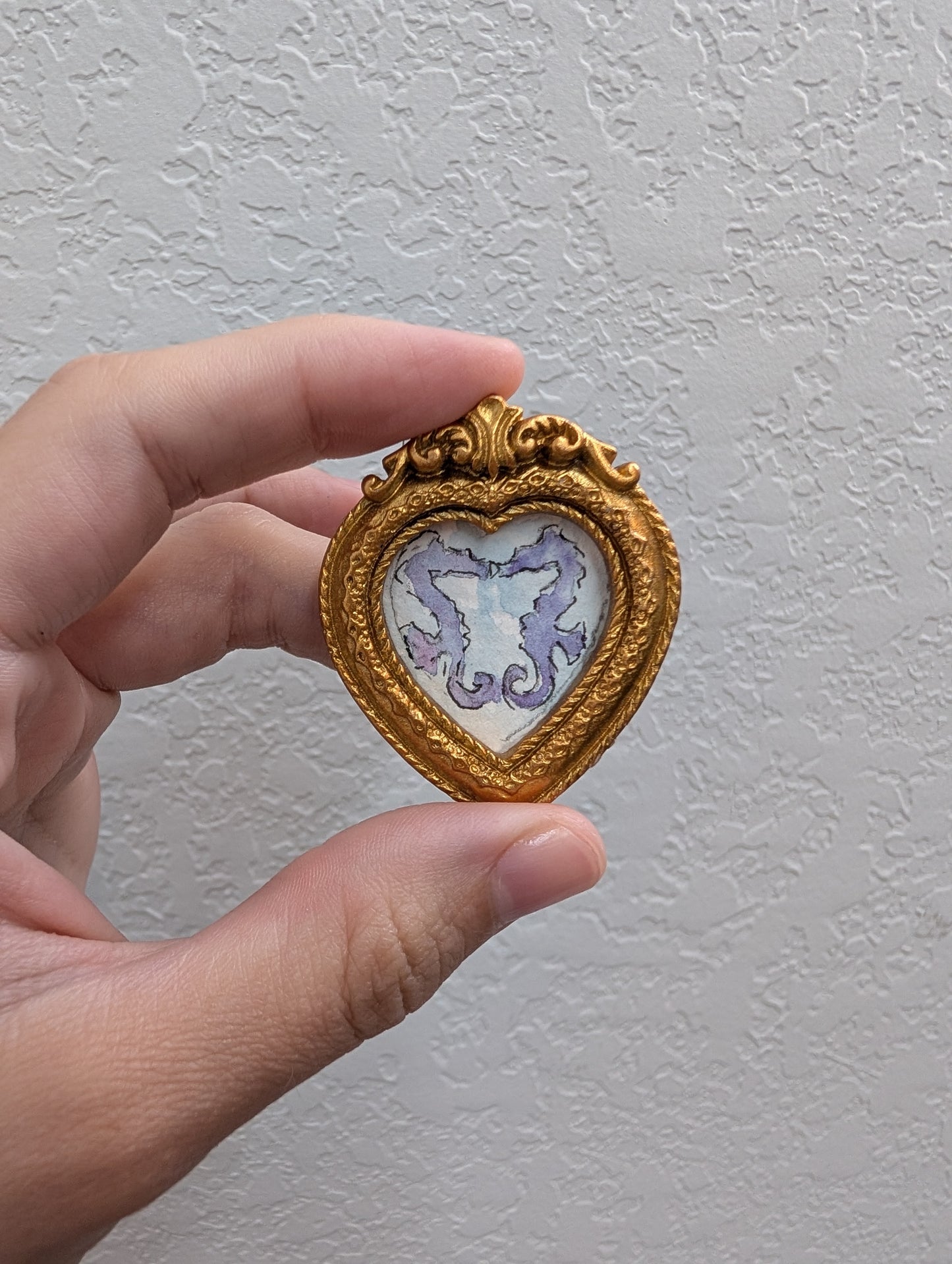 a hand holding a small heart shaped brooch