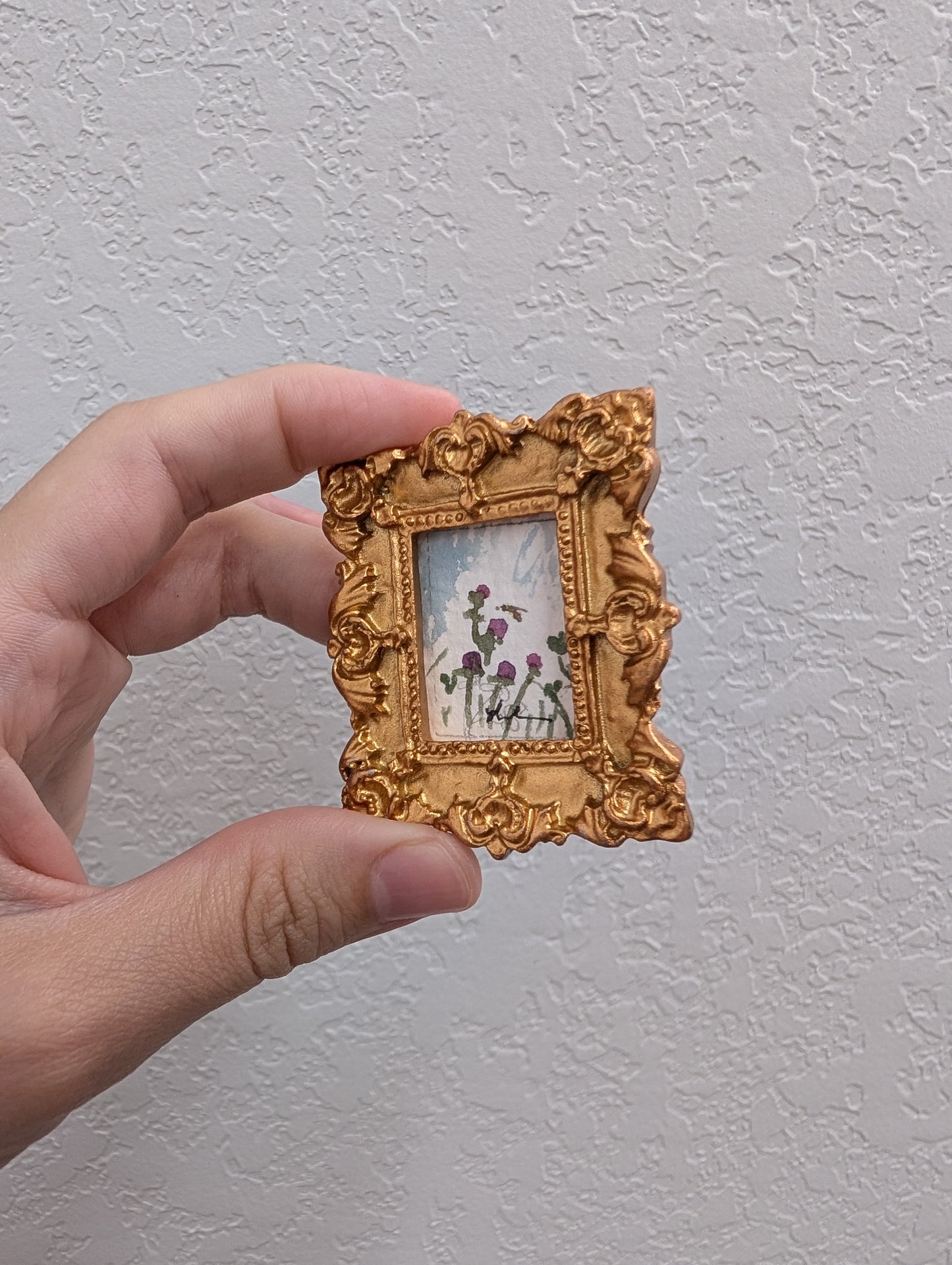 a hand holding a small picture frame with flowers on it