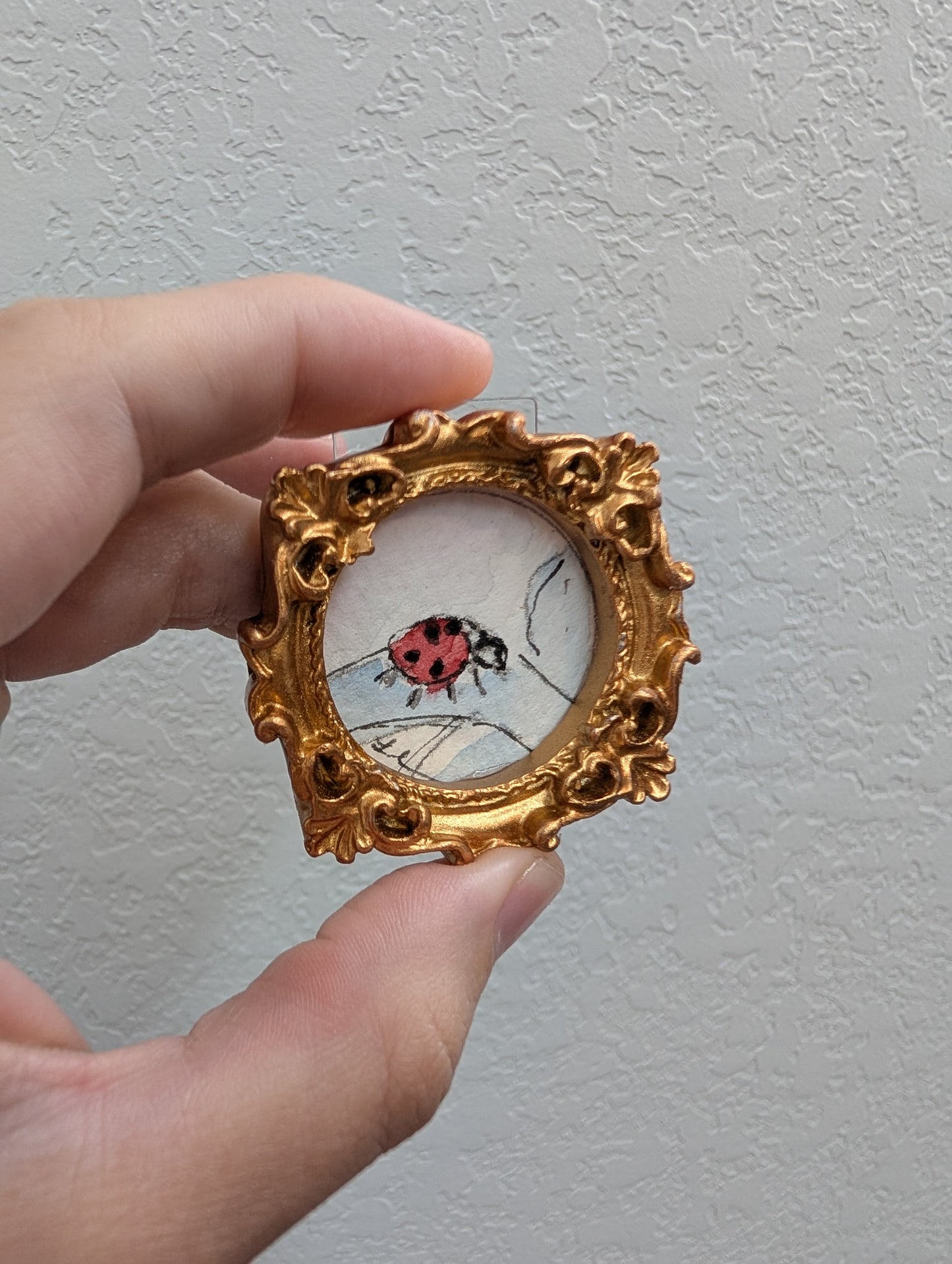 a hand holding a miniature picture of a ladybug