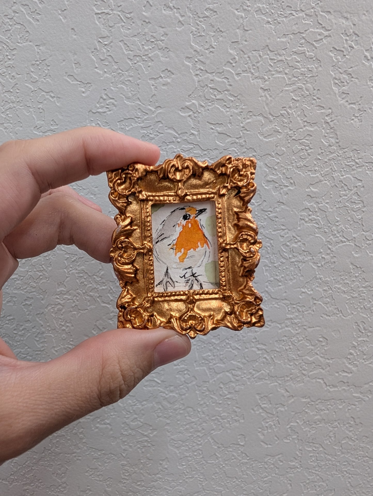 a hand holding a miniature gold frame with a picture of a bird