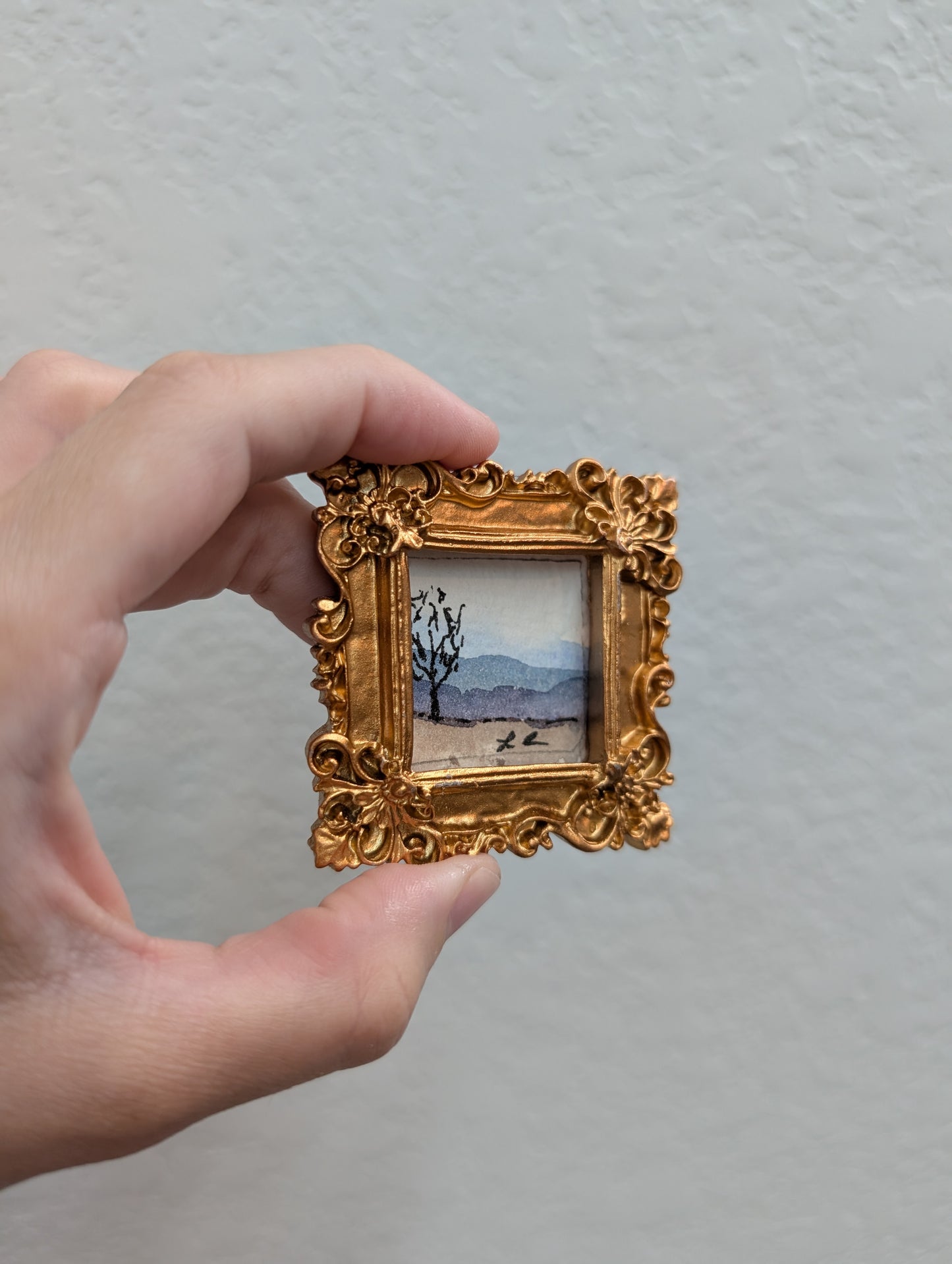 a person holding a small picture frame with a painting on it