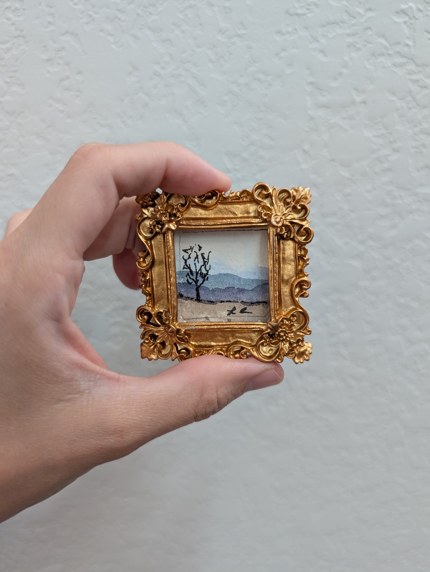 a person holding a picture of a tree in a gold frame