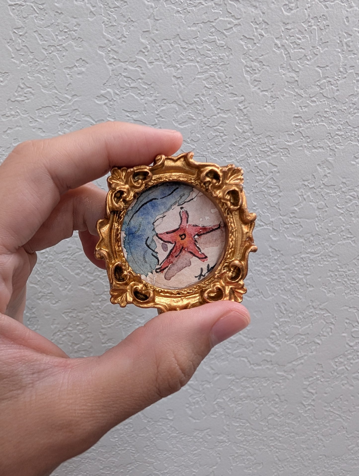 a hand holding a miniature picture of a starfish