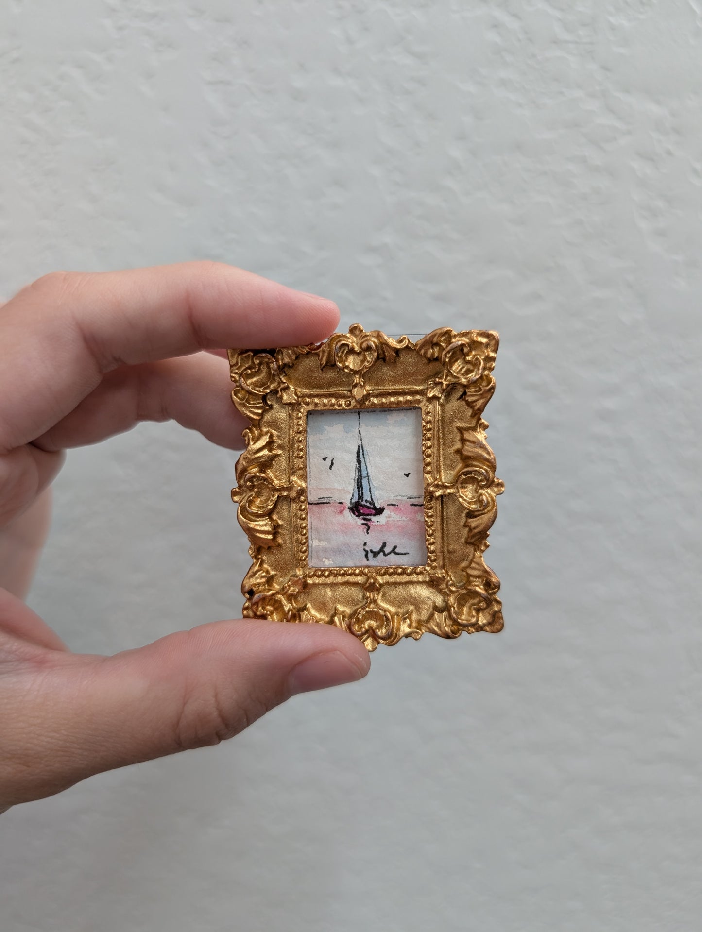 a person holding a small picture frame with a sailboat on it