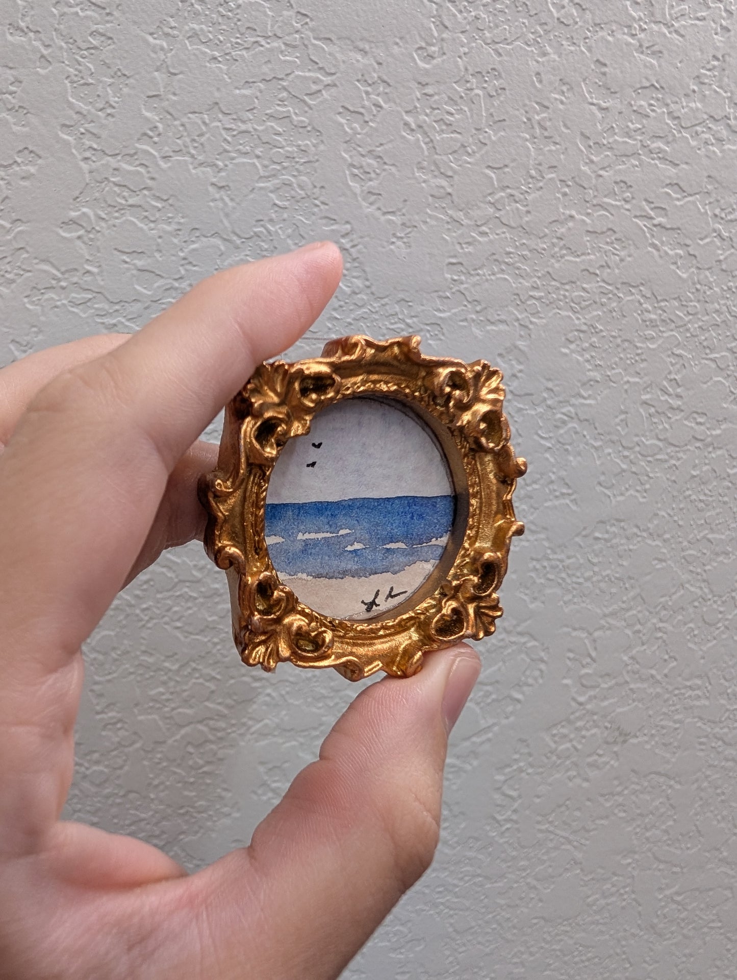 a hand holding a miniature picture frame with a painting on it