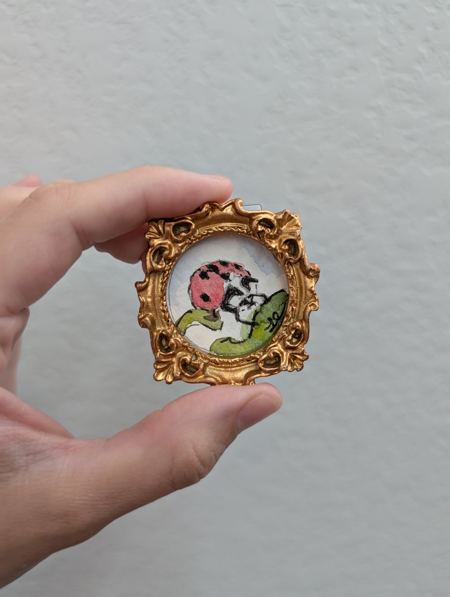 a hand holding a miniature picture of a ladybug