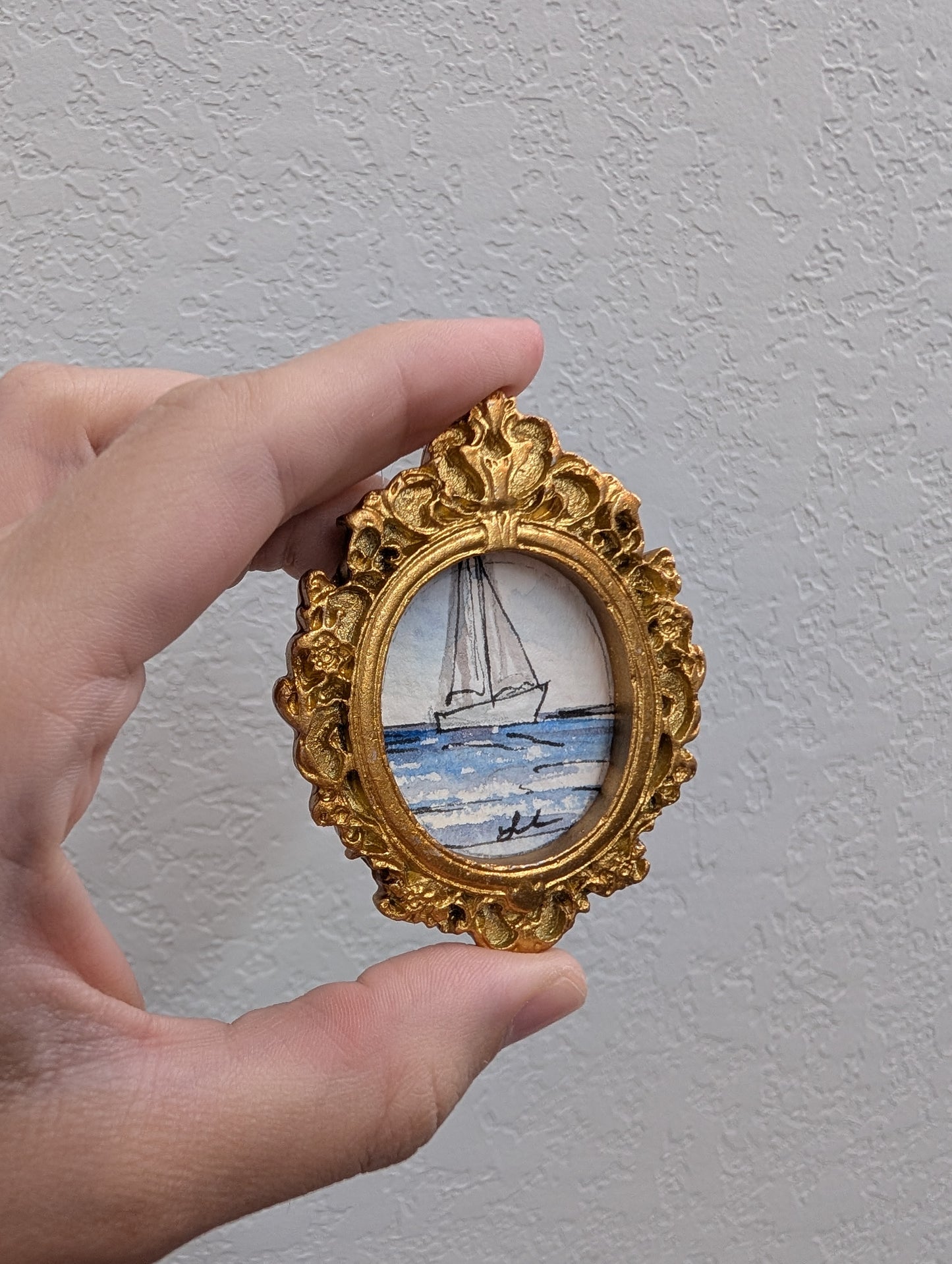 a hand holding a miniature picture of a sailboat