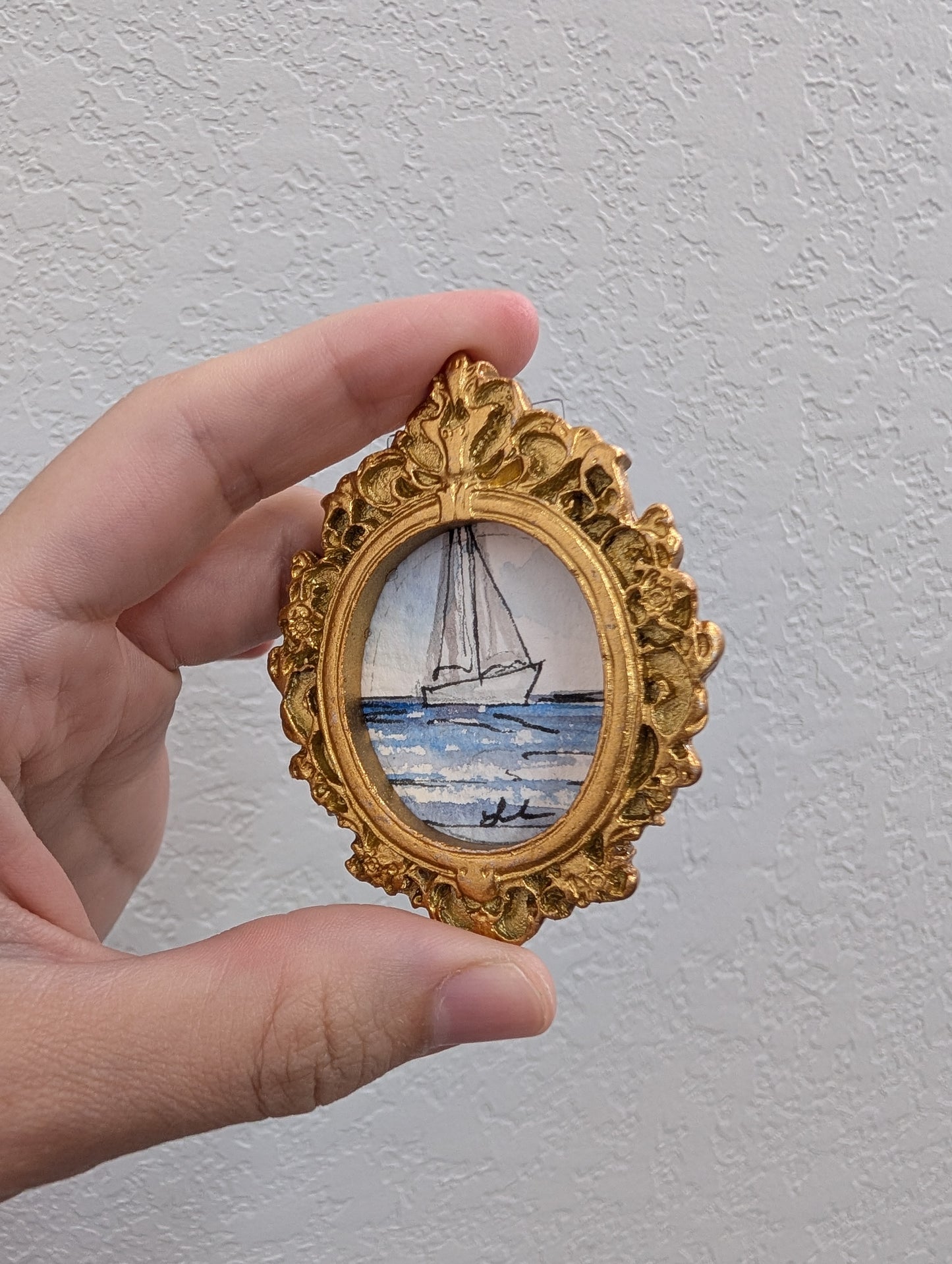 a hand holding a miniature picture of a sailboat