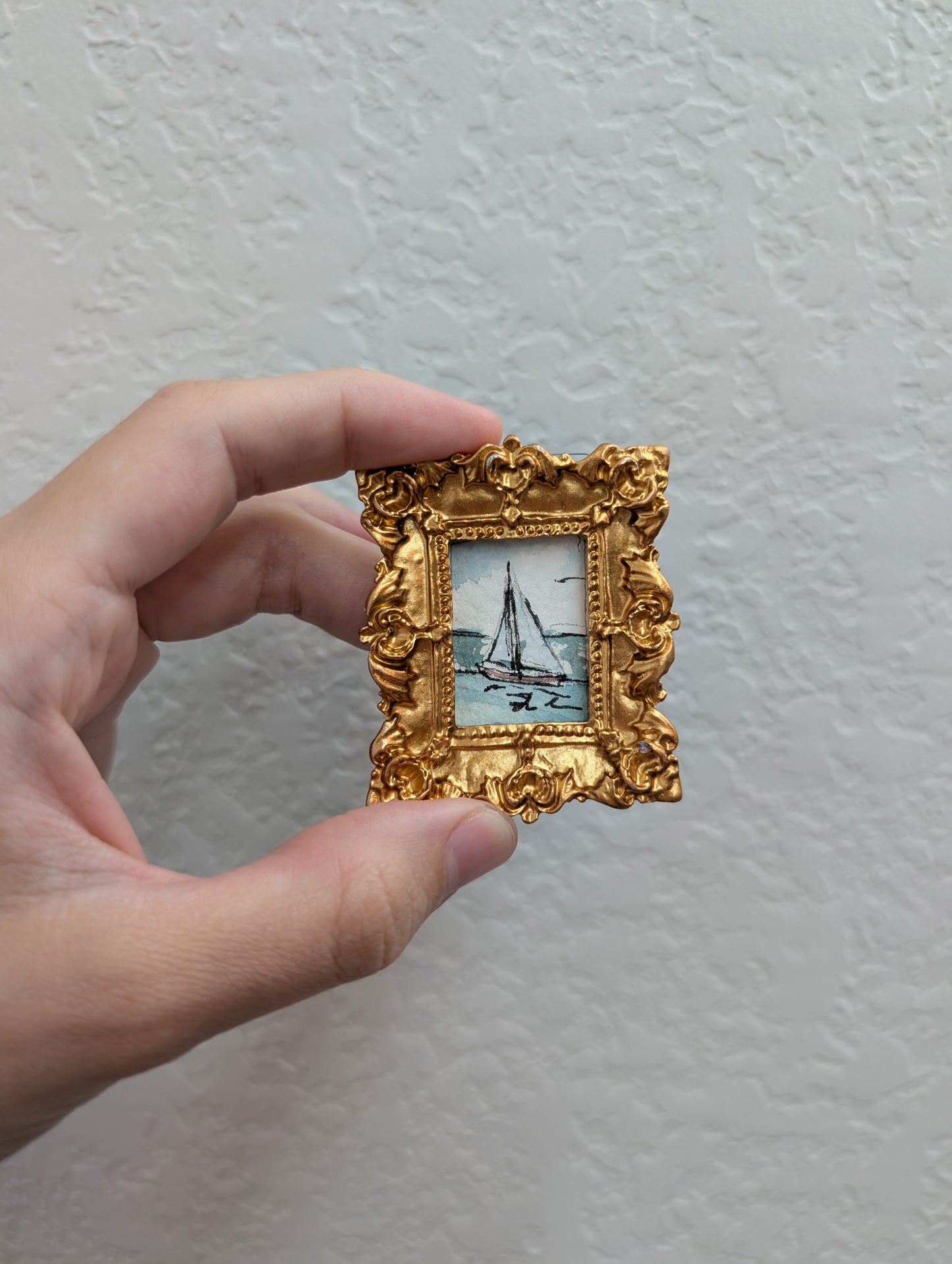 a hand holding a miniature picture frame with a sailboat on it