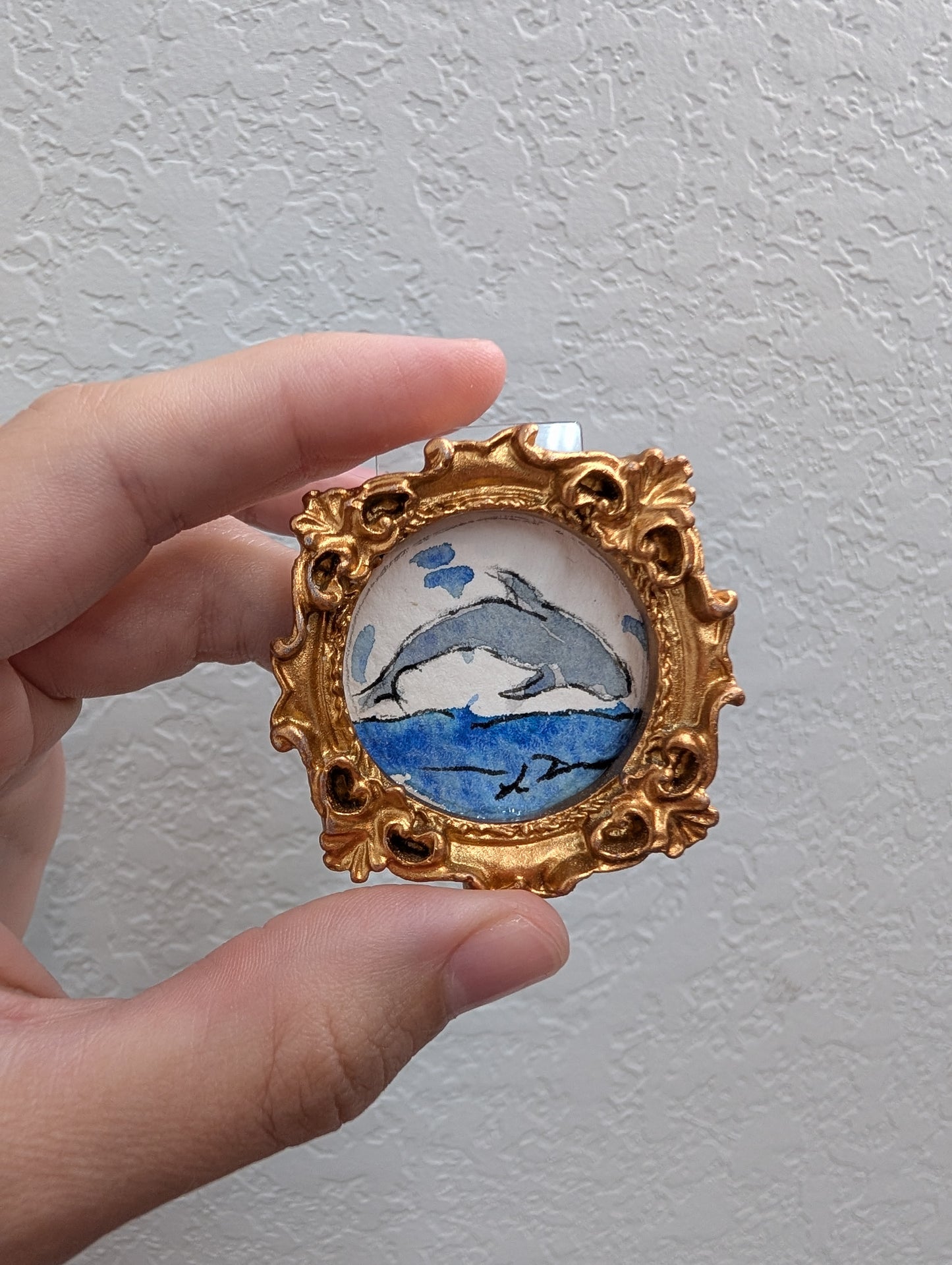 a hand holding a miniature picture frame with a dolphin on it