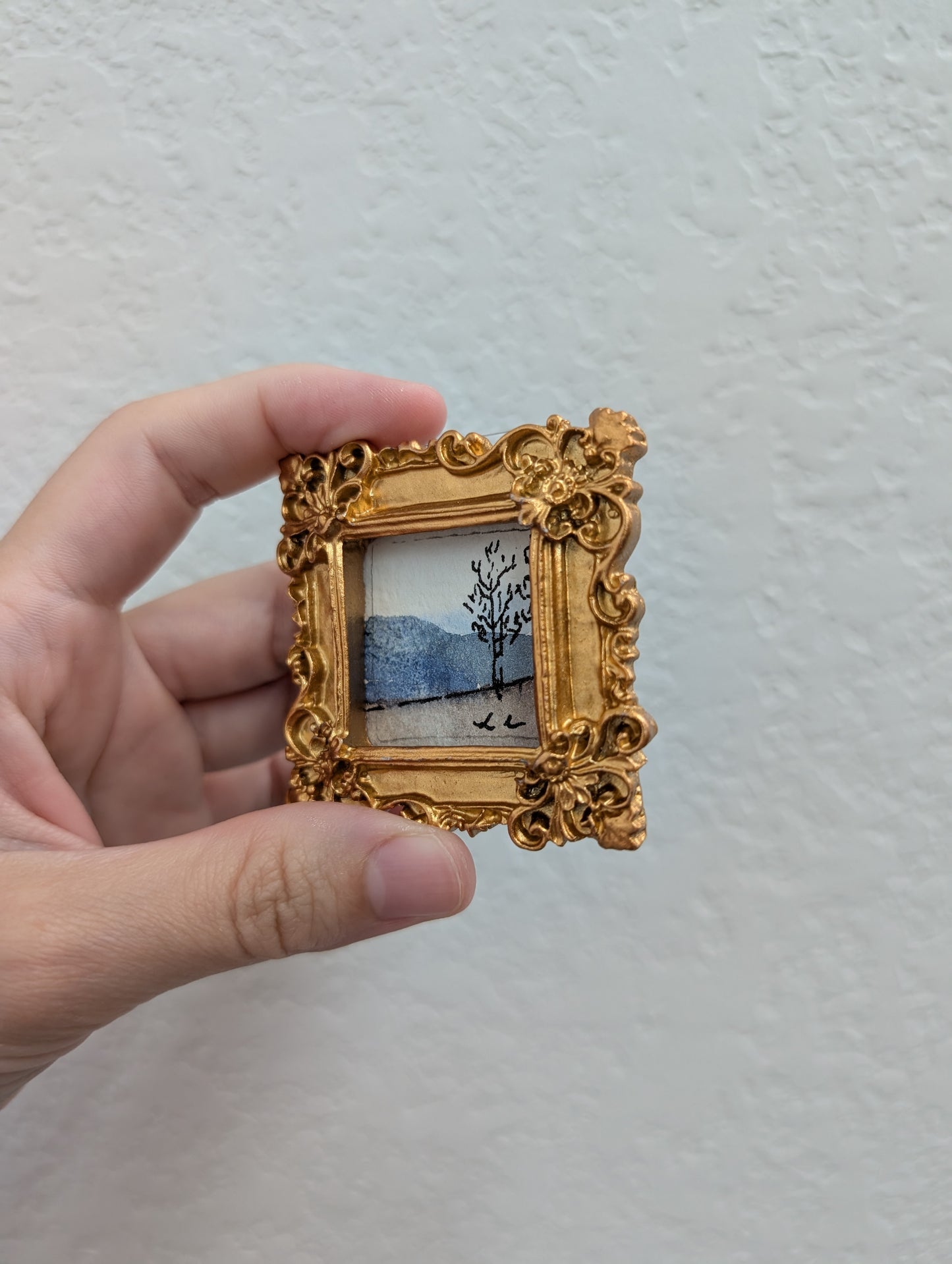a person holding a small picture frame with a painting on it