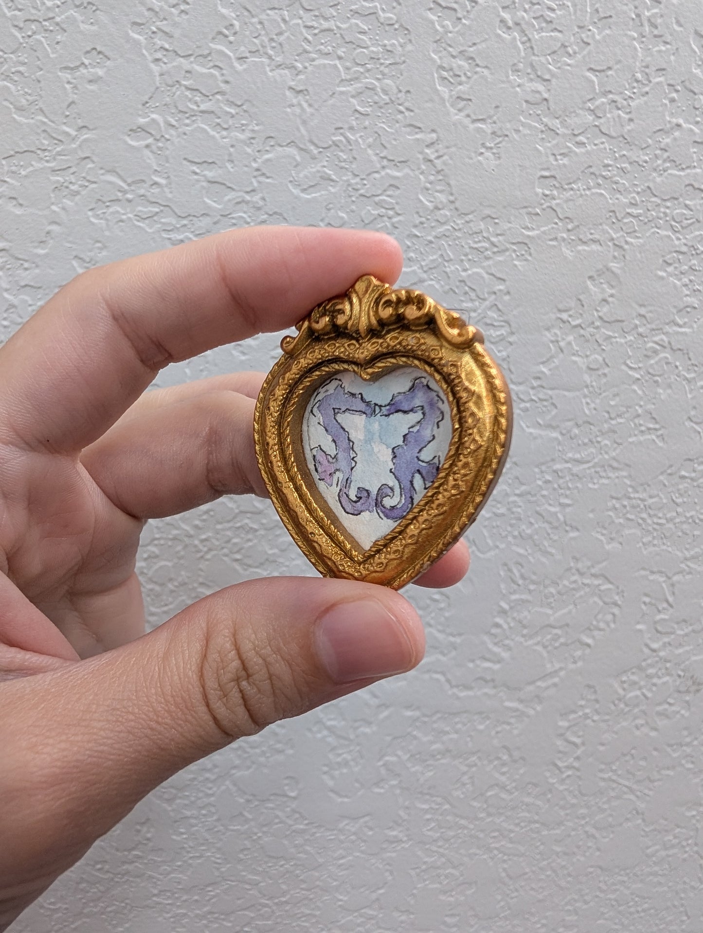 a hand holding a small heart shaped brooch