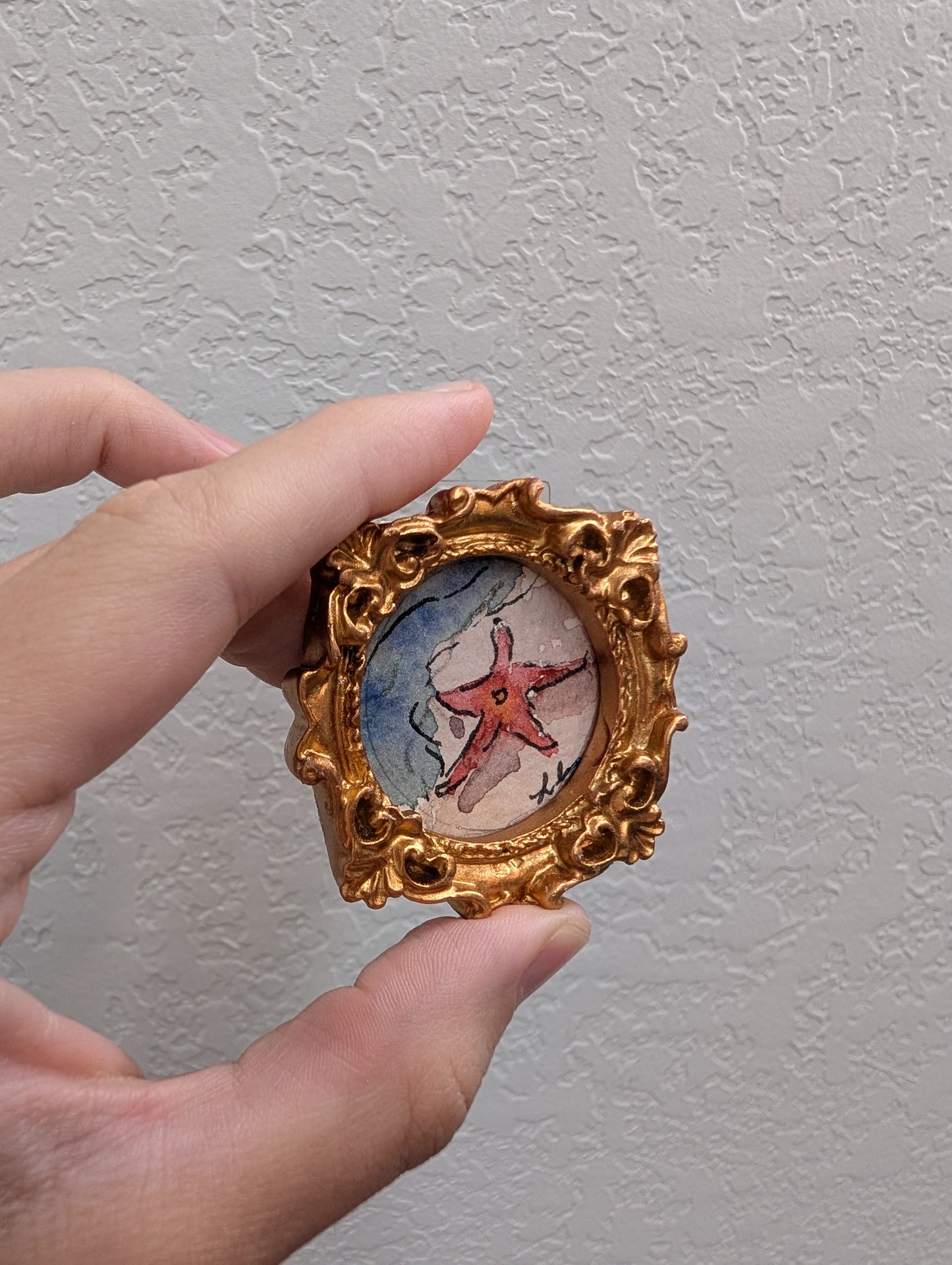 a hand holding a miniature picture of a starfish
