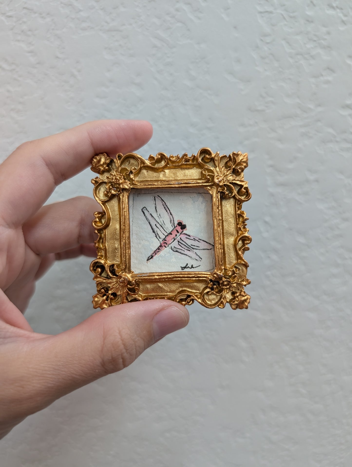 a hand holding a miniature picture of a dragonfly