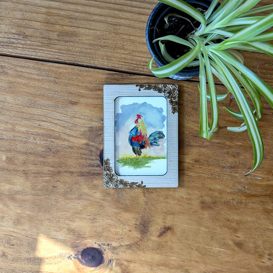 a picture of a rooster on a card next to a potted plant