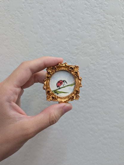 a hand holding a miniature picture of a ladybug
