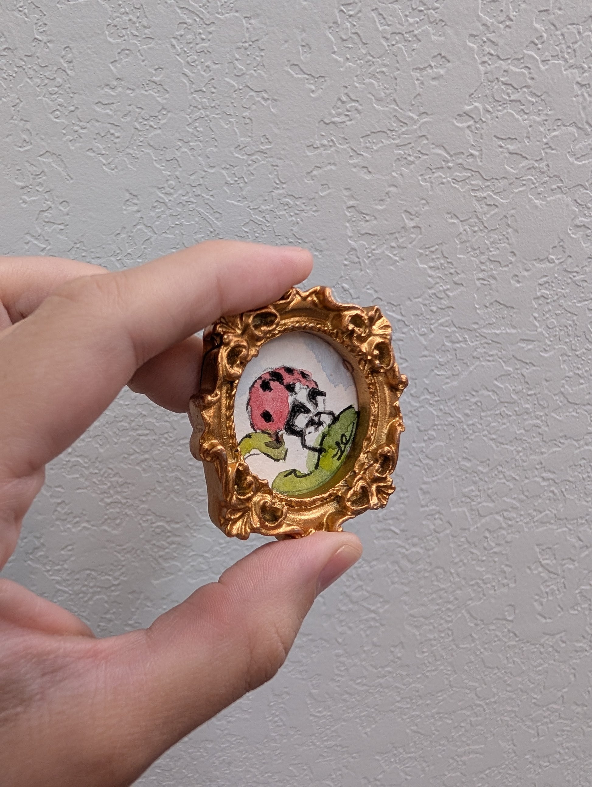 a hand holding a small picture frame with a ladybug on it