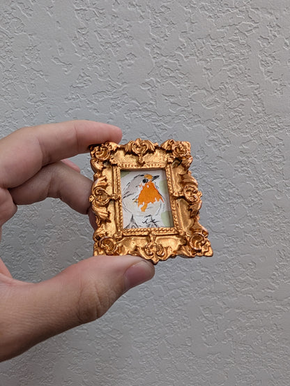 a hand holding a miniature picture frame with a picture of a bird on it