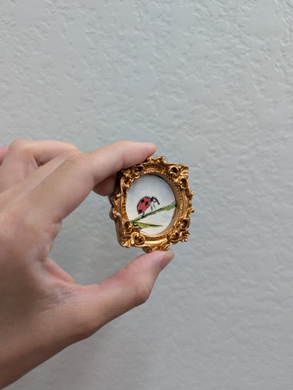 a hand holding a miniature picture frame with a ladybug on it