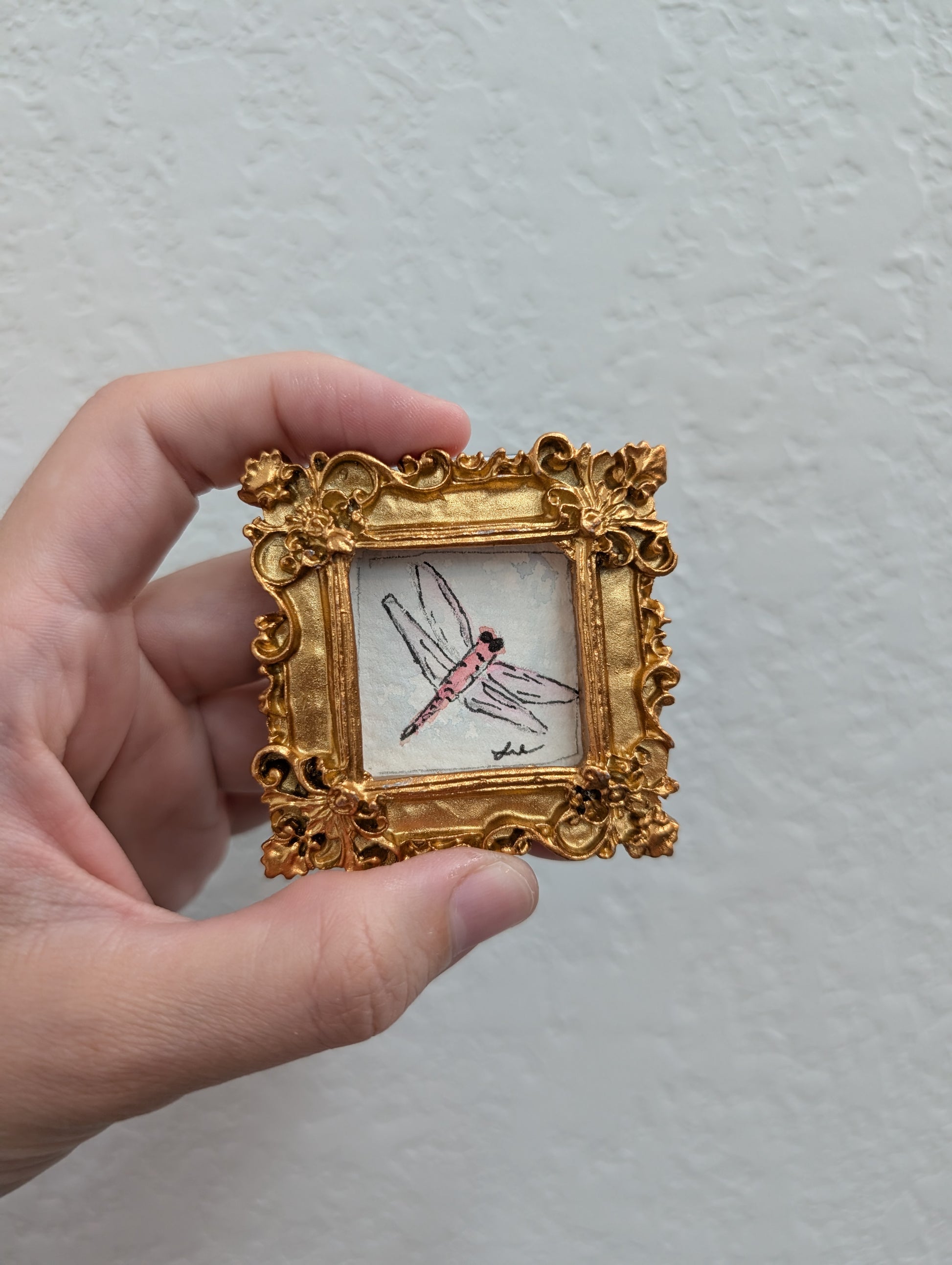 a hand holding a miniature picture of a dragonfly