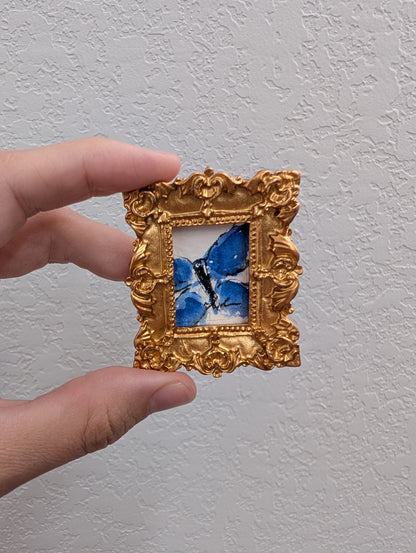 a hand holding a small picture frame with a blue butterfly on it