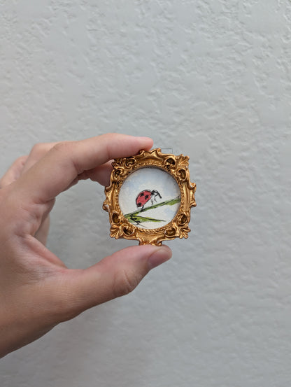 a hand holding a small picture frame with a ladybug on it