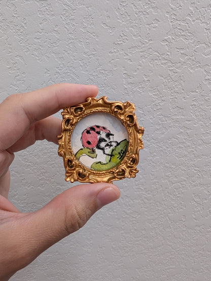 a hand holding a picture frame with a picture of a ladybug on it