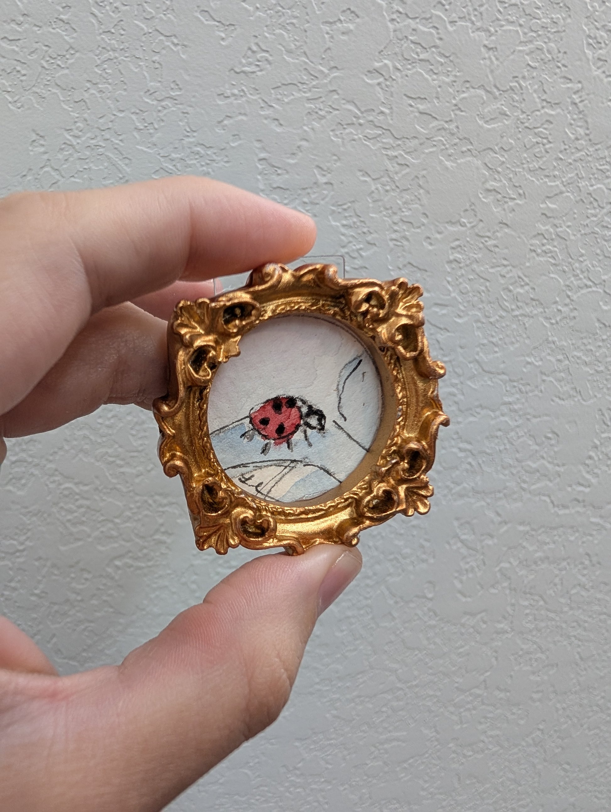 a hand holding a miniature picture of a ladybug