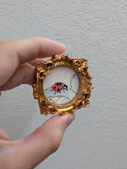 a hand holding a miniature picture of a ladybug