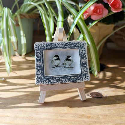 a picture of two birds sitting on top of a wooden easel