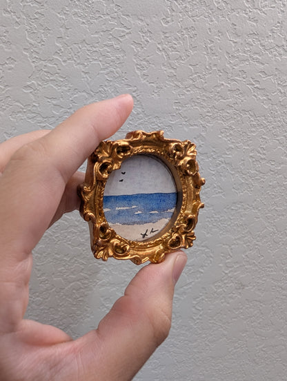 a hand holding a miniature picture frame with a painting on it
