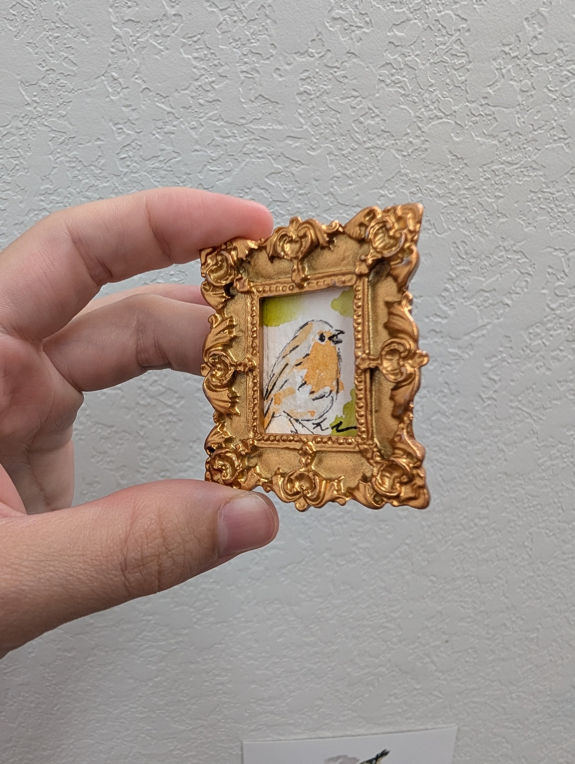 a hand holding a miniature picture of a bird